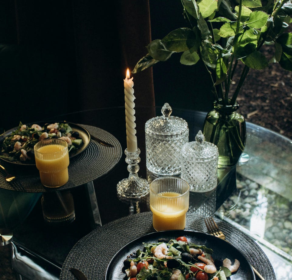 Elegant dining setup with salad, orange juice, candle, and white roses on a table.